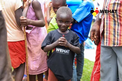 Ugandan boy wearing WEHAT Foundation NGO t-shirt holding a lolipop