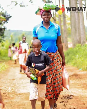 Ugandan boy wearing WEHAT Foundation NGO t-shirt walking with his mother